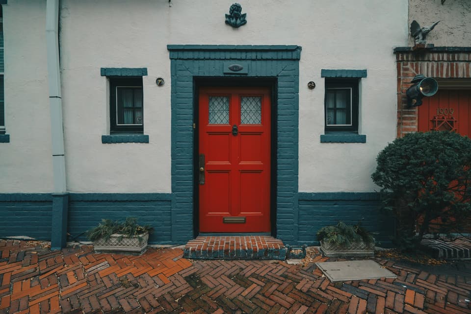 A red front door with a brass lock in a painted brick doorway