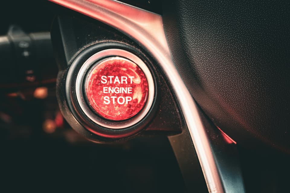 A red Start Engine Stop button beside a car steering wheel