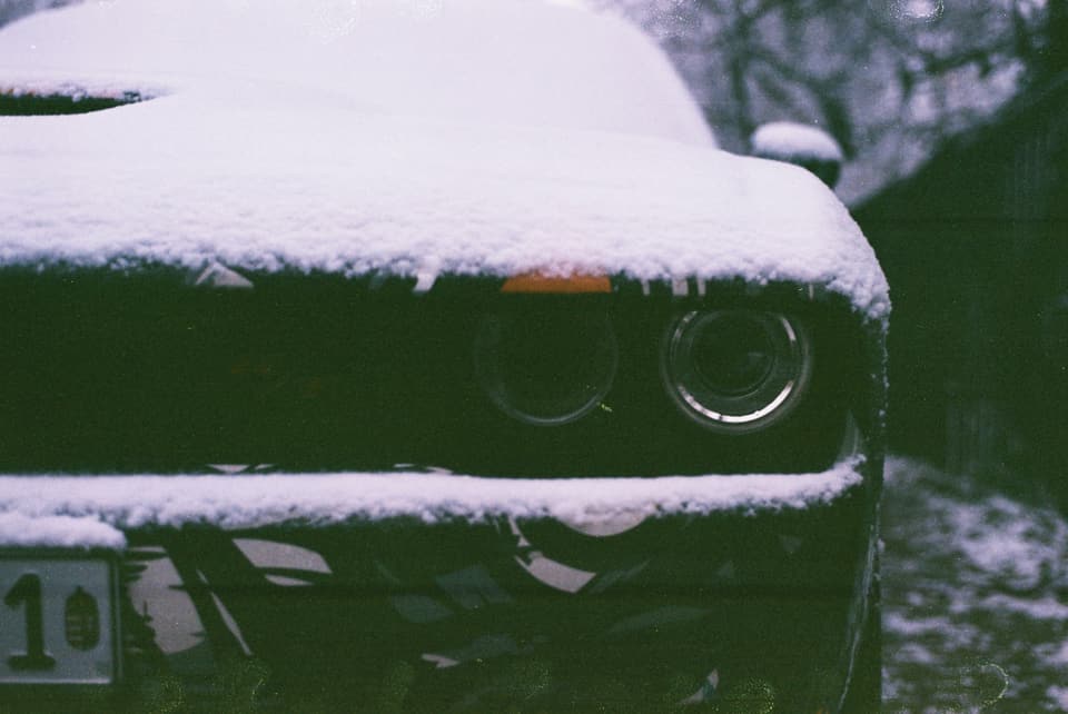 The snow-covered front of a dark car